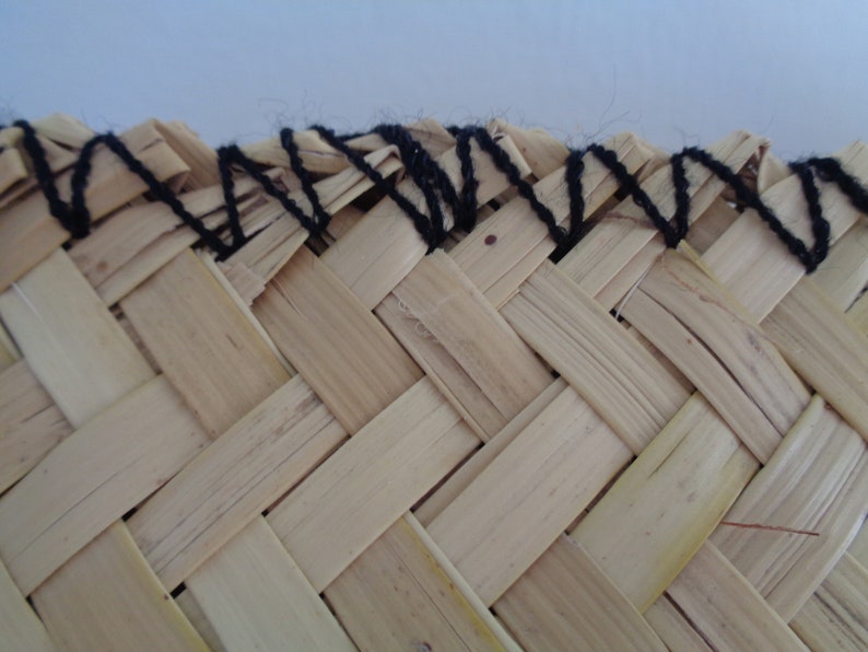 May include: Close-up of a woven straw hat with a black yarn trim around the edge.