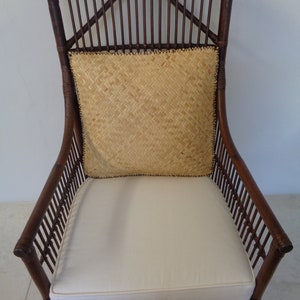 May include: A brown wicker armchair with a white cushion and a woven straw pillow. The chair has a high back and arms.