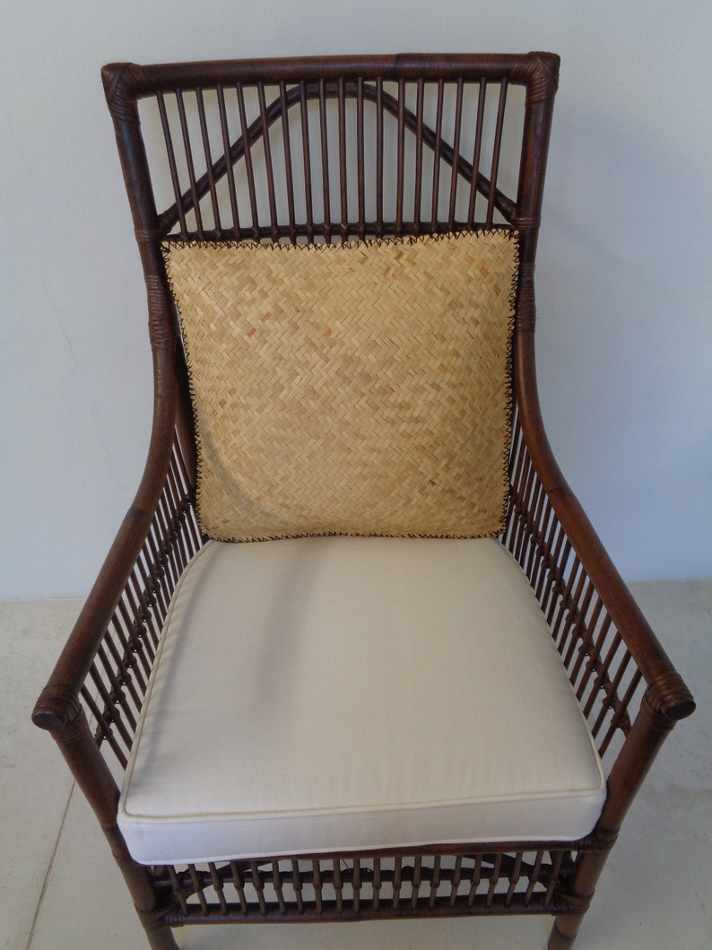 May include: A brown wicker armchair with a white cushion and a woven straw pillow. The chair has a high back and arms.