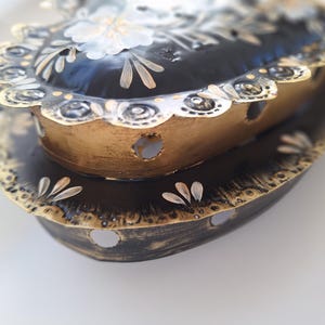 Puede incluir: Portavelas decorativo de metal en forma de coraz&oacute;n, en negro y dorado. El portavelas tiene un borde festoneado y est&aacute; adornado con detalles florales. El dise&ntilde;o presenta una construcci&oacute;n en capas con agujeros recortados para que pase la luz.