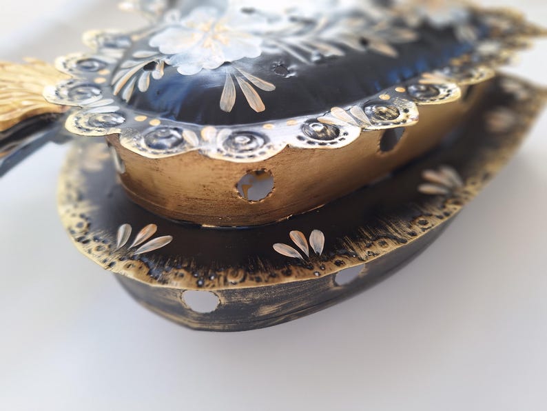Puede incluir: Portavelas decorativo de metal en forma de coraz&oacute;n, en negro y dorado. El portavelas tiene un borde festoneado y est&aacute; adornado con detalles florales. El dise&ntilde;o presenta una construcci&oacute;n en capas con agujeros recortados para que pase la luz.