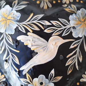 Puede incluir: Decoraci&oacute;n de pared en forma de coraz&oacute;n negro con un colibr&iacute; y un dise&ntilde;o floral. El colibr&iacute; est&aacute; pintado en blanco y crema, con detalles dorados y blancos en las flores y hojas. Los bordes son dorados.
