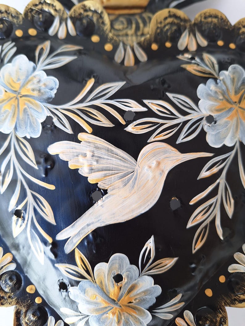 Puede incluir: Decoraci&oacute;n de pared en forma de coraz&oacute;n negro con un colibr&iacute; y un dise&ntilde;o floral. El colibr&iacute; est&aacute; pintado en blanco y crema, con detalles dorados y blancos en las flores y hojas. Los bordes son dorados.