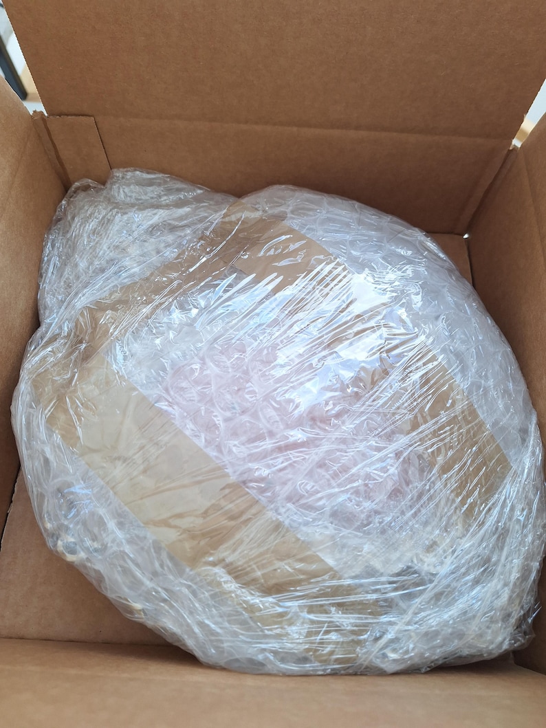 Puede incluir: Una caja de cart&oacute;n marr&oacute;n que contiene un art&iacute;culo envuelto. El art&iacute;culo est&aacute; protegido por film transparente y pl&aacute;stico de burbujas. El contenido es parcialmente visible a trav&eacute;s del embalaje.