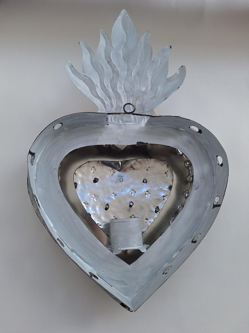 Puede incluir: Decoraci&oacute;n de pared met&aacute;lica en forma de coraz&oacute;n con dise&ntilde;o de llama en la parte superior. Pintada en tonos grises y plateados, con interior texturizado y un portavelas. Ideal para decoraci&oacute;n de interiores.