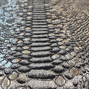 May include: Close-up of a black and silver fabric with a snakeskin pattern. The fabric has a textured, embossed look.