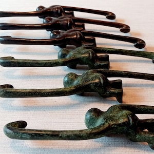 May include: A line of eight bronze monkey figurines, each with a curved tail, are arranged on a white surface. The monkeys are all facing the same direction, with their heads bowed and their tails curled up. The monkeys are all the same size and shape, but they are different shades of bronze.