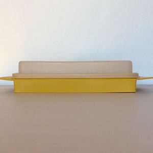 Peut inclure: Un beurrier en plastique jaune avec un couvercle transparent. Le beurrier est rectangulaire et a une surface lisse.