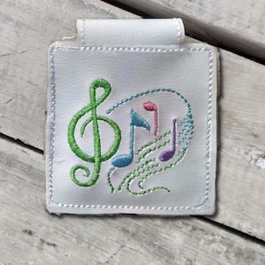 May include: White leather key chain with a green treble clef and colorful musical notes embroidered on it.