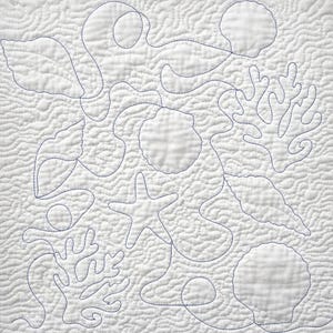 Pode incluir: Um edredom branco com um design de vida marinha. O edredom apresenta costuras azuis que delineiam várias criaturas marinhas, incluindo conchas, estrelas do mar e corais. O fundo tem um padrão texturizado e ondulado.