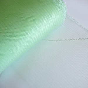 May include: A roll of light green tulle fabric with a scalloped edge. The fabric is sheer and has a delicate texture.