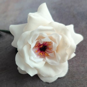 May include: A single white silk rose with a pink and orange center. The rose is in focus and the background is blurred.