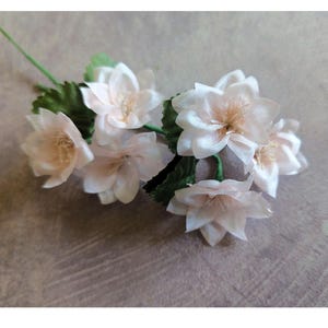 May include: A bunch of six delicate, pale pink silk flowers with green stems and leaves. The flowers have a slightly shimmery finish.