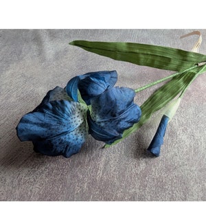 May include: A single artificial blue iris flower with green leaves. The flower has a spotted pattern.