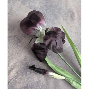 May include: A single artificial purple iris flower with green leaves. The flower is in bloom and has a white center.