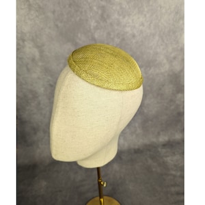 May include: A gold-colored, round, woven hat sits on a white mannequin head. The hat is made of a fine, delicate material.