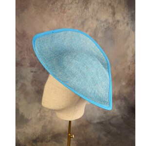 May include: A light blue hat with a wide brim and a blue trim. The hat is made of a woven material and is sitting on a display stand.