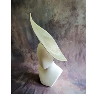 Puede incluir: Un sombrero grande, de color blanco roto, de ala ancha con una corona puntiaguda. El sombrero está hecho de un material tejido y tiene un acabado liso ligeramente texturizado.