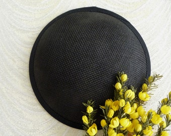 May include: A black, round, woven hat with a black trim. The hat is sitting on a white textured surface.