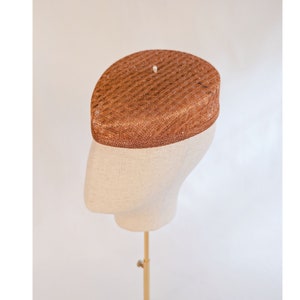 May include: A brown woven hat with a rounded shape, sitting on a white mannequin head.