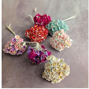 May include: A collection of small, colorful artificial flower bouquets. The bouquets are in shades of red, pink, purple, blue, and cream, with yellow centers. Each bouquet has a small stem.