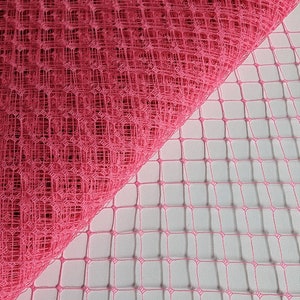 May include: Pink netting fabric with a square grid pattern. The fabric is folded in half, showing the texture of the netting.