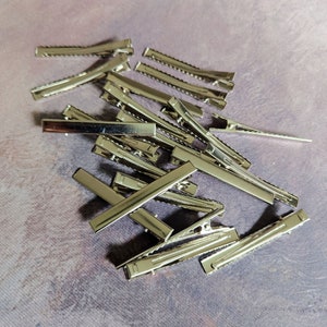 May include: A pile of silver metal hair clips. The clips are all the same size and shape, and they are arranged in a random pattern.