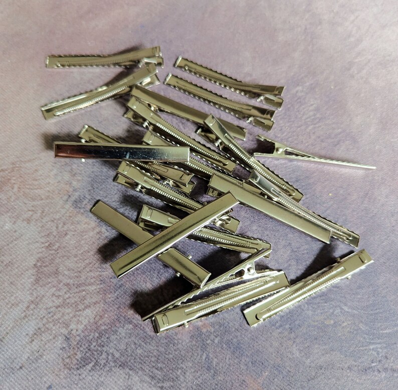 May include: A pile of silver metal hair clips. The clips are all the same size and shape, and they are arranged in a random pattern.