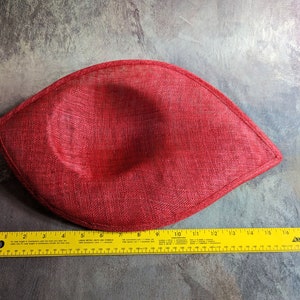May include: A red fabric hat with a rounded shape and a slightly pointed tip. The hat is measured with a ruler, showing it is about 18 inches long.