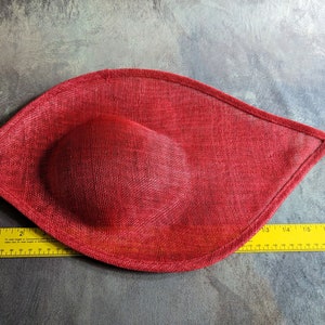 May include: A red fabric hat with a rounded shape. The hat is made of a textured material and has a smooth, rounded top.