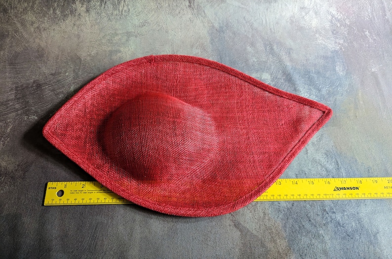May include: A red fabric hat with a rounded shape. The hat is made of a textured material and has a smooth, rounded top.