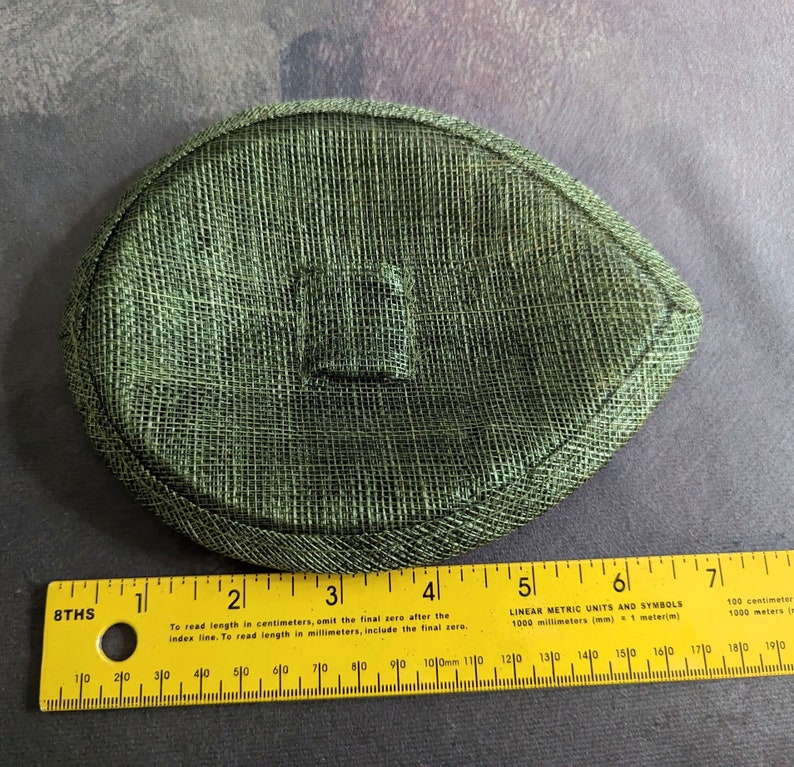 May include: A green oval-shaped hat made of a woven material. The hat is approximately 5 inches in diameter.