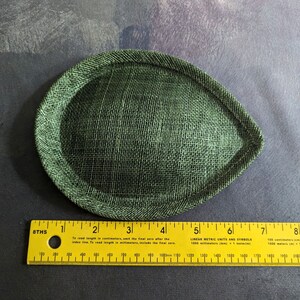 May include: A green fabric hat base, measuring approximately 12 cm in diameter, with a stitched edge.