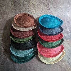 May include: A stack of 10 round, hat-shaped, fabric pieces in various colors, including brown, beige, teal, navy, red, green, and black. The fabric pieces are arranged in two stacks of five.