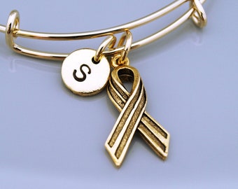 May include: Gold expandable bracelet with a gold ribbon charm and a gold charm with the letter "S" engraved on it.