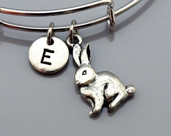 Könnte beinhalten: Ein silbernes, verstellbares Armkettchen mit einem silbernen Anhänger in Form eines Kaninchens und einem silbernen Anhänger mit dem Buchstaben E.