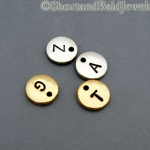 May include: Four metal letter beads, two gold and two silver, with the letters "N", "A", "T", and "G" on them. The beads are used for jewelry making.
