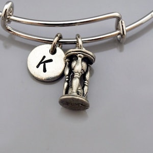 May include: A silver expandable bracelet with a charm of an hourglass and a silver charm with the letter K.