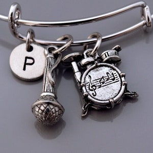 Könnte beinhalten: Silbernes Charm-Armband mit Mikrofon-, Schlagzeug- und Noten-Anhängern. Das Armband hat auch einen Anhänger mit dem Buchstaben "P" darauf.