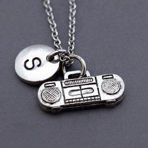 May include: Silver necklace with a charm of a vintage boombox and a silver disc charm with the letter 'S' engraved on it.