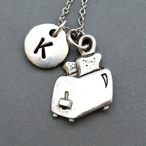 May include: Silver necklace with a charm of a toaster and a round charm with the letter K.