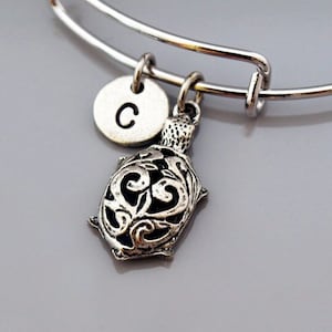 May include: Silver charm bracelet with a silver turtle charm and a silver disc charm with the letter C engraved on it.