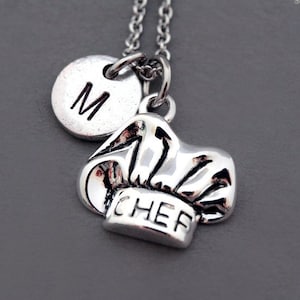 May include: Silver necklace with a chef hat charm and a round charm with the letter "M" on it.
