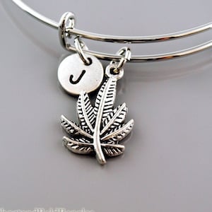 May include: A silver expandable bracelet with a silver charm of a marijuana leaf and a silver disc charm with the letter J.