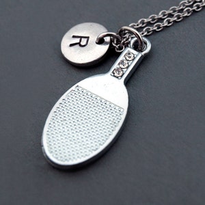 Puede incluir: Collar de plata con un dije de raqueta de tenis de mesa y un dije de plata con la letra R. El dije de raqueta tiene diamantes de imitación en la parte superior.