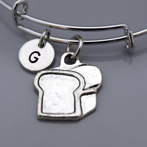May include: A silver charm bracelet with a bread charm and a silver charm with the letter G.