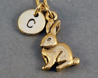 May include: Gold necklace with a small gold rabbit charm and a round gold charm with the letter C engraved on it.