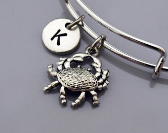 May include: Silver charm bracelet with a crab charm and a personalized disc with the letter K.
