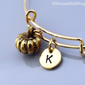 May include: Gold charm bracelet with a small gold pumpkin charm and a gold disc charm with the letter K engraved on it.