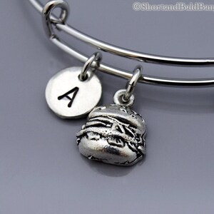 Puede incluir: Un brazalete de plata con un dije de hamburguesa y un dije con la letra A.